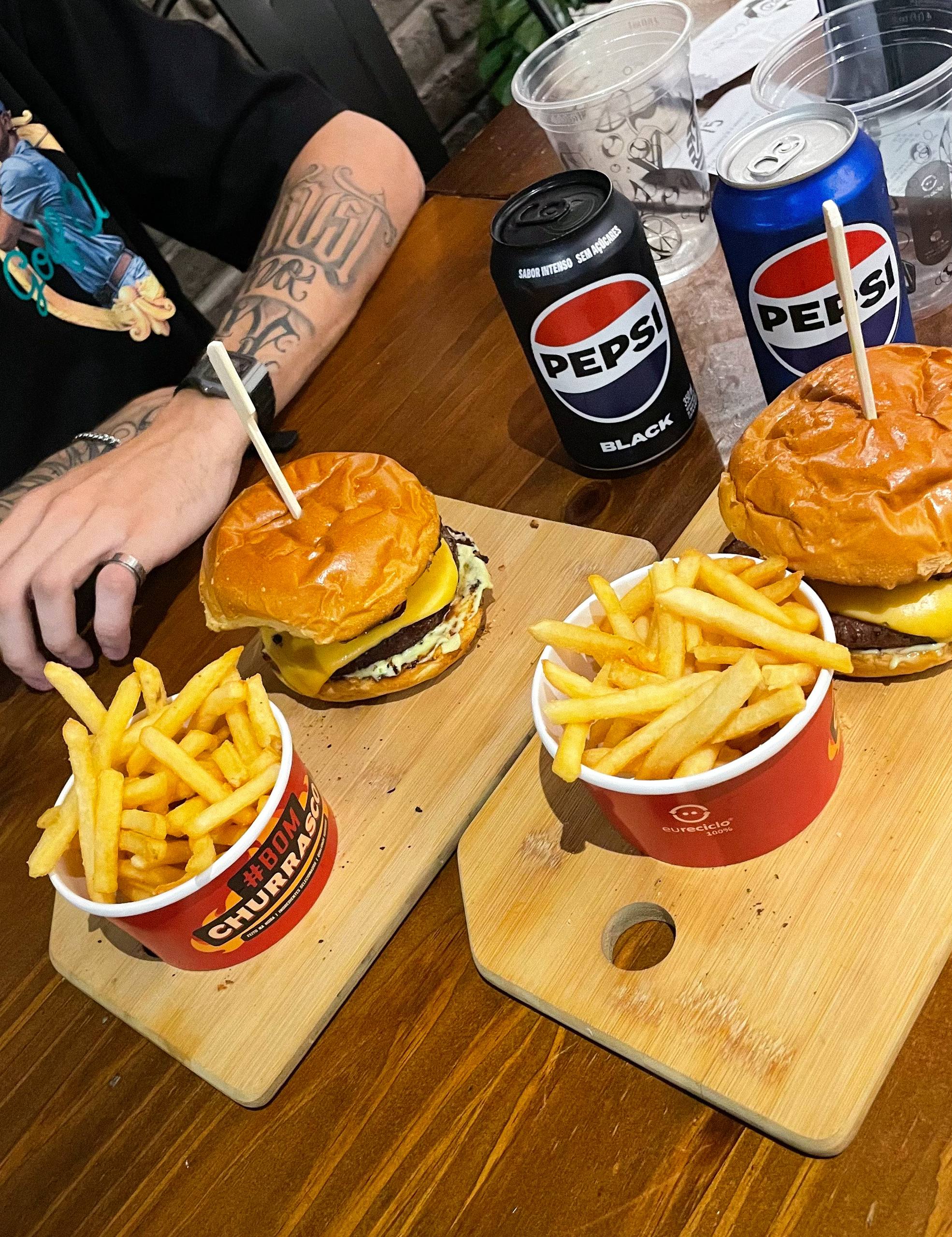 dois lanches com batatas ao lado e duas latas de refrigerante