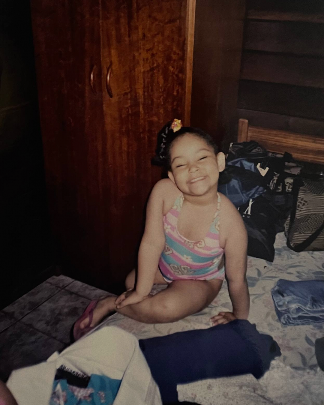 Foto minha criança, de maiô, sentada na cama,